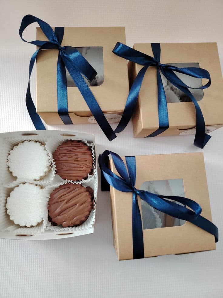 Cajas marrones con lazos azules y alfajores de chocolate y azúcar glas en caja abierta.