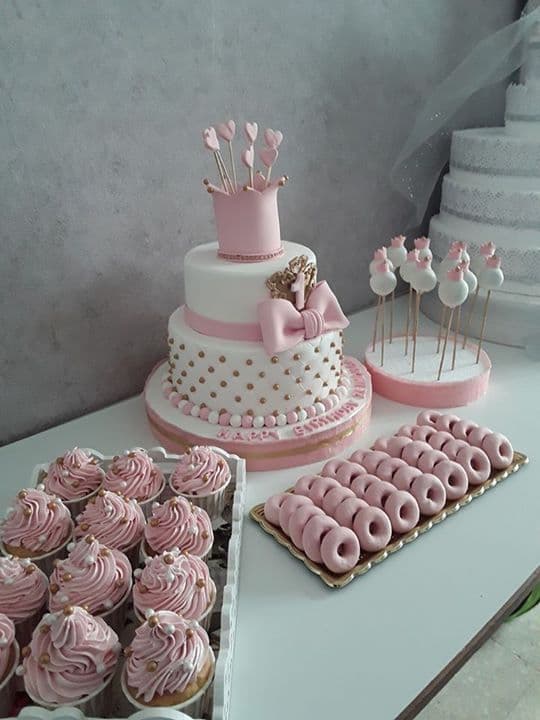 Pastel de tres pisos rosa y blanco con corona, cupcakes, mini donas y cake pops.