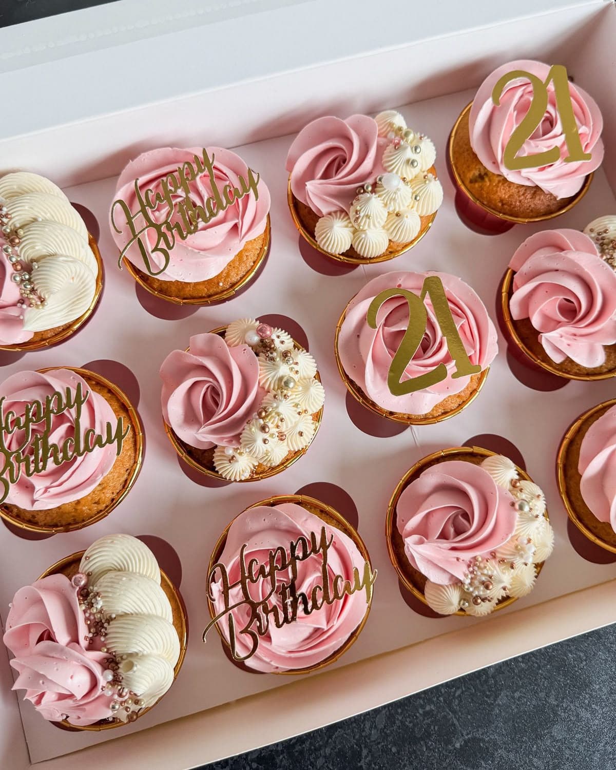 Cupcakes con rosas de crema rosa y blanca, adornos dorados de cumpleaños y número veintiuno.