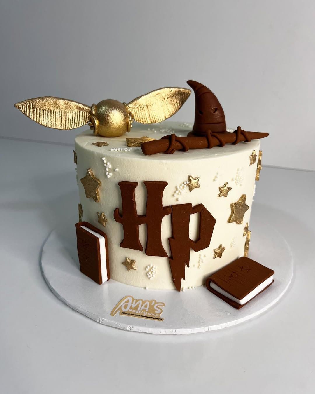 Pastel blanco de Harry Potter con snitch dorada, sombrero seleccionador, varita y estrellas decorativas.