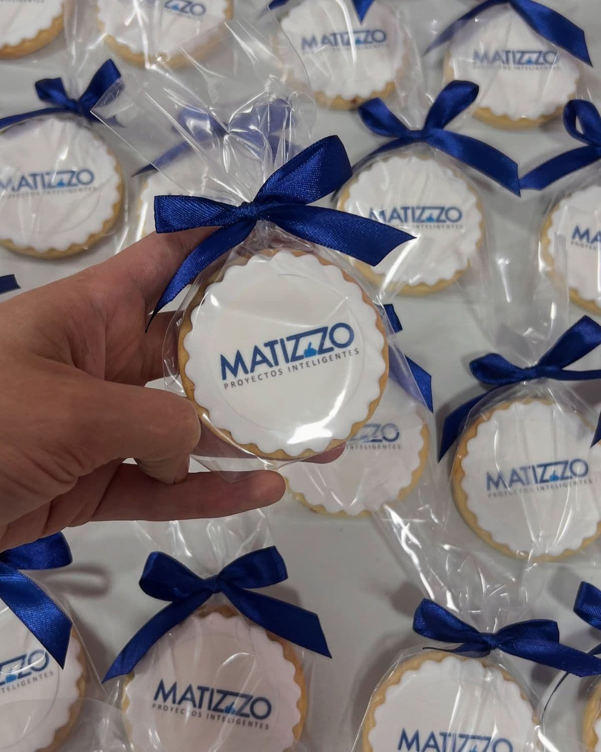 Mano sosteniendo una galleta con logo de Matizzo, envuelta en plástico con lazo azul.