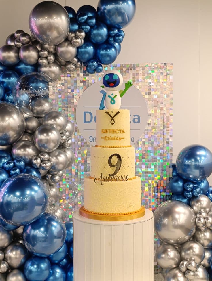 Pastel de tres niveles para noveno aniversario con robot, rodeado de globos azules y plateados.