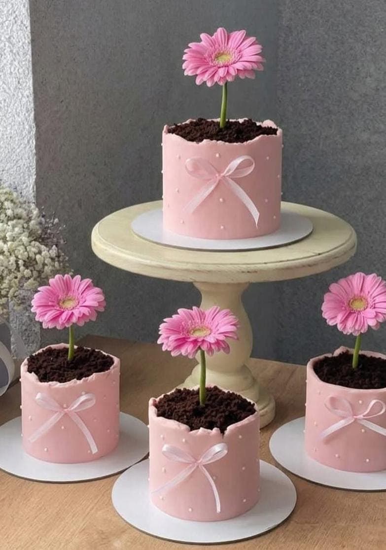 Pasteles rosas decorados como macetas con tierra de chocolate y margaritas rosas en el centro.